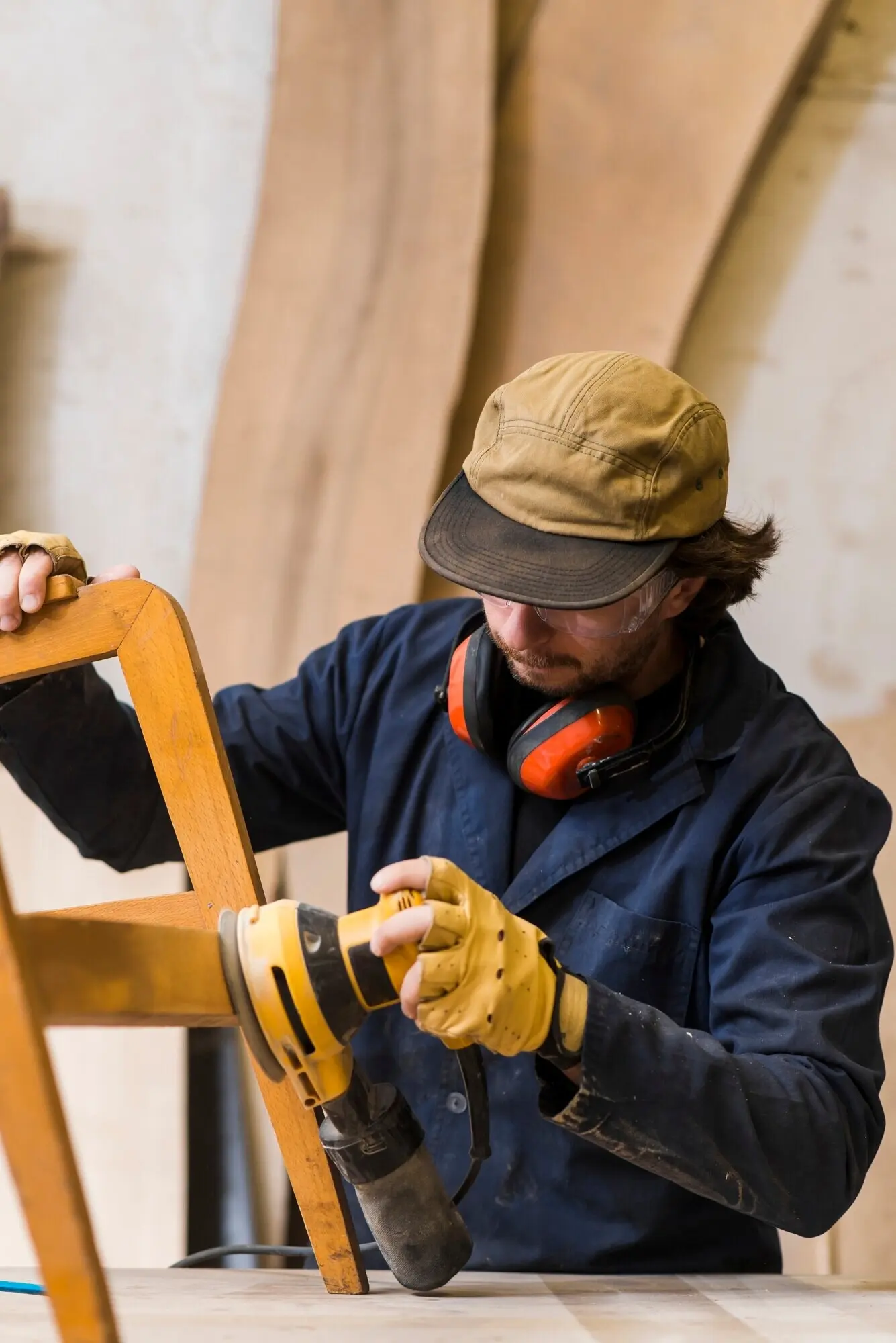 Close-up view of a male carpenter using a power tool to sand furniture on a workbench.